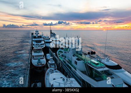Transport großer, teurer Yachten über den Ozean, auf einem Transportschiff, bei Sonnenuntergang. Stockfoto