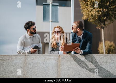 Drei Kollegen diskutieren Ideen, während sie an einem sonnigen Tag im Freien interagieren Stockfoto