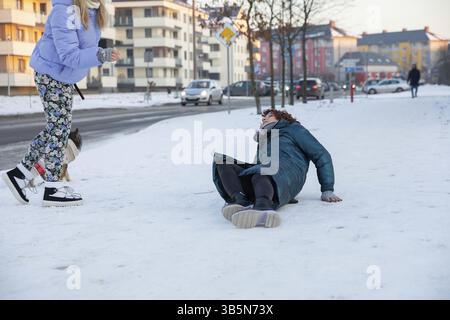 Eine Frau liegt im Schnee und kann nicht aufstehen. Sie ist umgefallen und ihr Bein tut weh. Eine zweite Frau geht auf sie zu und will ihr helfen. Ein kleines Stockfoto