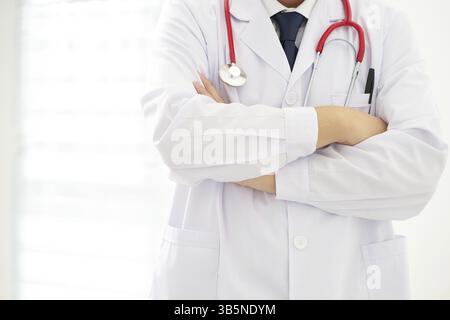 Unbekannter Arzt posiert mit überkreuzten Armen im Büro und trägt ein Stethoskop Stockfoto