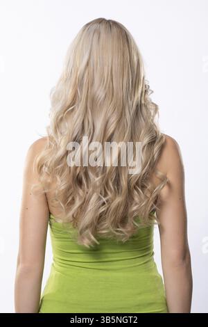 Eine Frau mit langen, welligen blonden Haaren ist elegant in einem leuchtend grünen Kleid gekleidet, von der Rückseite aus gesehen Stockfoto