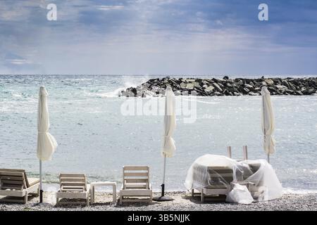 Drei gefaltet Sonnenschirme und Liegen am Strand mit stürmischen Meer im Hintergrund Stockfoto