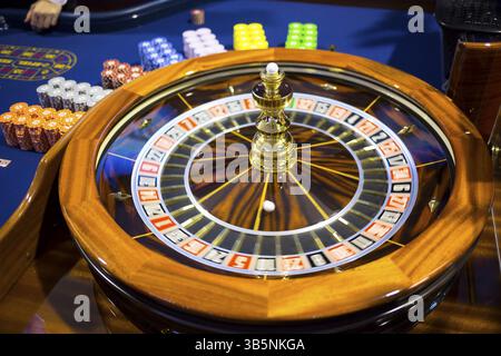 Hölzerne, farbenfrohe Kasino-Roulette. Spielautomat und Spielausrüstung. Roulette-Tisch mit Chips neben dem Roulette. Drehendes Roulette in Bewegung Stockfoto