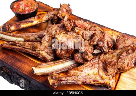 Saftige gegrillte Schweinerippchen sind wunderschön auf einer Holzplatte angeordnet, begleitet von einer frischen Salsa. Das Gericht zeigt eine lebendige Präsentationsidee Stockfoto