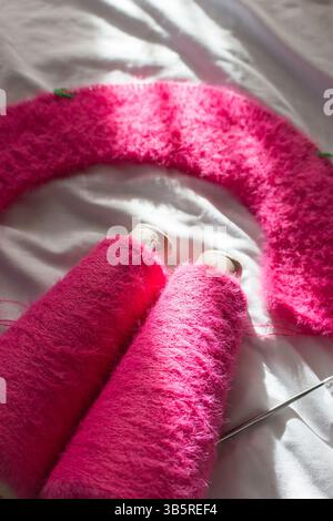 Hellrosafarbenes Stricken mit Stricknadeln auf weißem Laken. Weiche rosafarbene Strickmode mit runden Nadeln. Hintergrund des Strickmusters. Strick Lifestyle. Stockfoto