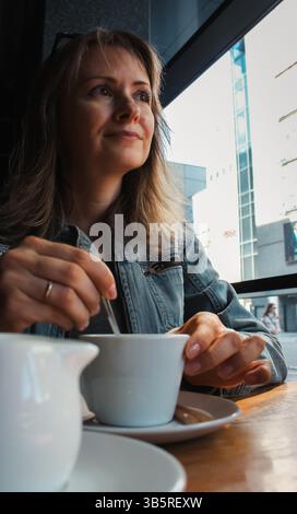 Schöne Frau, die Kaffee im Café trinkt. Tageskonzept. Genießen Sie Ihr Lebenskonzept. Brünette, die Milch in Americano rührt. Gemütlicher Lifestyle. Stockfoto