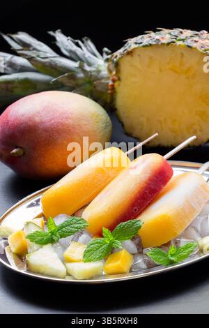 Mangobanaseis auf einem dekorativen Teller mit zerstoßenem Eis und frischem Obst. Eine reife Mango und eine halbe Ananas verstärken das t Stockfoto