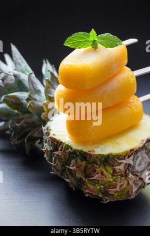 Spalte von Sorbet-Eis-Eis-Eis von Ananas auf Hälfte Ananas auf schwarzem Hintergrund. Ananassorbet-Eis-Eis. Vertikal. Schließen. Stockfoto