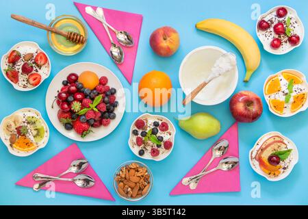 6 Schüsseln Joghurt mit verschiedenen Zutaten Obst, Beeren, Nüssen, Honig und 6 Löffeln, Servietten auf hellblauem Hintergrund. Sechs verschiedene Wagnisse Stockfoto