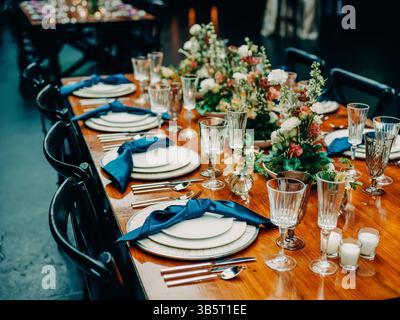 Schauen Sie sich den eleganten Esstisch an, der mit Blumen, Gläsern und Besteck geschmückt ist und für die Abendgäste bereit ist. Stockfoto