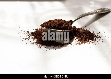 Alter Löffel mit gemahlenem Kaffee im Sonnenlicht, Aroma des Tagesanfangs, verstreut gemahlener Kaffee Stockfoto