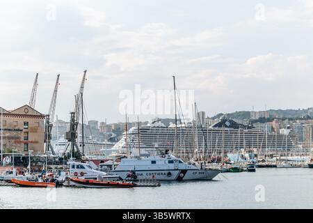 Genua, Italien - 22. September 2024: Küstenwache Boote, Segelboote und ein großes Kreuzfahrtschiff legen im geschäftigen Hafen mit der Skyline der Stadt an. Stockfoto