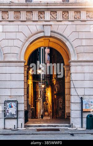 Genua, Italien - 22. September 2024: Historischer Steinbogen führt in eine enge mittelalterliche Gasse, die von Laternen beleuchtet wird, im Herzen der Altstadt Stockfoto