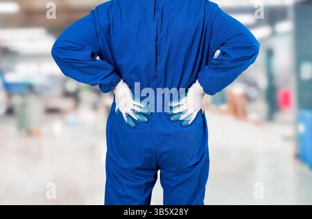 Rückansicht eines nicht erkennbaren Mechanikers, der seinen unteren Rücken aufgrund von Schmerzen im Werk unangenehm hält Stockfoto