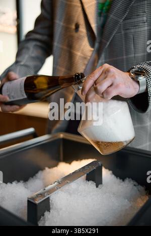 Sektverkostung, der Sommelier gießt Sekt aus der Flasche in den Dekanter, Sektblasen, Nische mit Eis Stockfoto