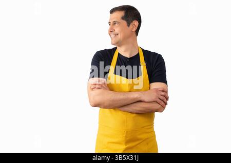 Der Verkäufer steht über einem isolierten weißen Hintergrund und blickt zur Seite und denkt mit gelber Schürze davon Stockfoto