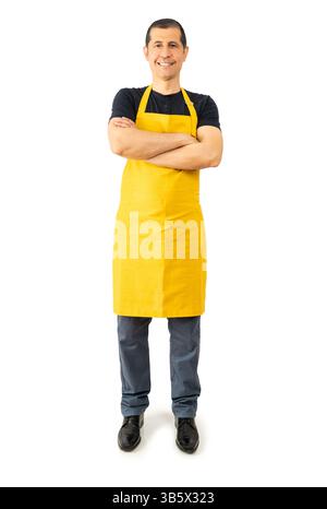 Aufnahme in voller Länge von selbstbewusstem Supermarkt-Mitarbeiter mit überkreuzten Armen und gelber Schürze auf weißem Hintergrund Stockfoto