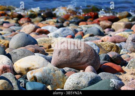 Farbenfrohe, glatte Kieselsteine an einem steinigen Ostseestrand mit flachem blauem Wasser im Hintergrund, gefangen in hellem natürlichem Sonnenlicht. Stockfoto