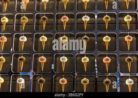 Eine lebendige Anordnung von Eiskegeln hängt an einer schlanken Wand mit einer Vielzahl von Farben und Texturen. Jeder Kegel hat einen anderen Geschmack, cre Stockfoto