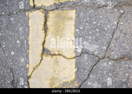 Gerissener Asphaltpflaster mit verblasster gelber Linie auf der Straße Stockfoto