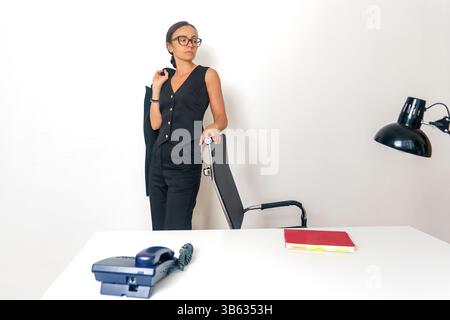Eine ernsthafte Geschäftsfrau in einem schwarzen Anzug steht am Tisch und lehnt sich mit den Händen darauf Stockfoto
