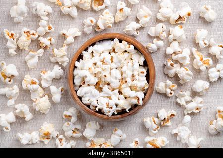 Frisches Popcorn, gepuppter Mais in einer Holzschale und rundherum, auf Leinenstoff. Samen der Sorte Zea mays everta, erweitert und aufgebläht. Stockfoto