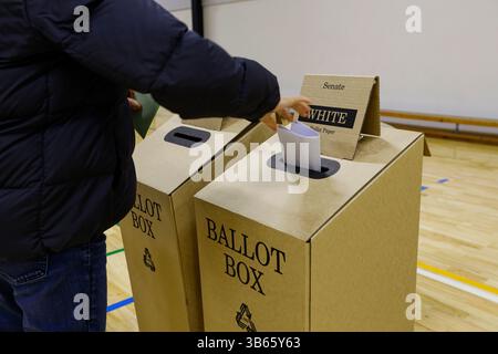 Ein Wähler legt seine Stimmzettel am Wahltag während der australischen Bundestagswahl in eine Wahlbox in einem Wahlzentrum. Am Wahltag des 3. Mai 2025 gaben die Wähler der Division of Hotham ihre Stimmzettel an Wahllokalen ab, darunter am Killester College in Springvale. Der Sitz des Labour-Abgeordneten Clare O'Neil seit 2013 wird von dem liberalen Kandidaten Harmick Singh Matharu, dem Grünen-Kandidaten Martin Barry und anderen umstritten. Zu den zentralen Themen der Wähler zählen der Druck auf die Lebenshaltungskosten, die Erschwinglichkeit des Wohnraums und die Entwicklung der Infrastruktur. Hotham umfasst eine vielfältige, multikulturelle Bevölkerung im Südosten und im Südosten Stockfoto