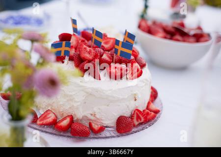 Eine Nahaufnahme eines Tischsets mit einem Kuchen aus Erdbeeren und Schlagsahne und einer Schüssel Erdbeeren im Hintergrund Stockfoto