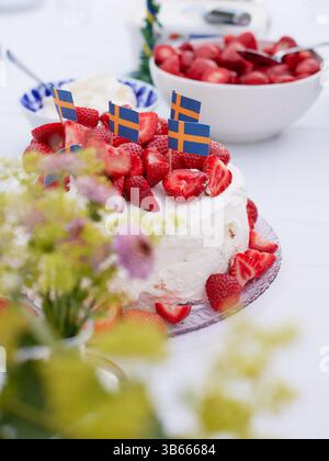 Eine Nahaufnahme eines Tischsets mit einem Kuchen aus Erdbeeren und Schlagsahne und einer Schüssel Erdbeeren im Hintergrund Stockfoto