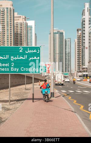 Dubai, VAE - 30. April 2026: Asiatischer Migrant Worker auf den Straßen von Dubai. Hochwertiges fotooffenes Bild eines asiatischen Arbeitsmigranten, der auf einer Straße in Dubai, Vereinigte Arabische Emirate, spaziert. In Arbeitskleidung unter der intensiven Sonne des Nahen Ostens verkleidet, repräsentiert der Mann die hart arbeitenden Einwanderer, die die rasante Stadtentwicklung der Stadt unterstützen. Das Foto zeigt Themen wie Globalisierung, Arbeitsmigration und Alltag in einer modernen Metropole. Stockfoto