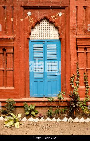 Symmetrische Fassade aus freiliegendem rotem Backstein mit bogenförmigen Ornamenten und blauen Fensterläden, typisch für die spätkoloniale Stadtarchitektur von Dhaka. Stockfoto