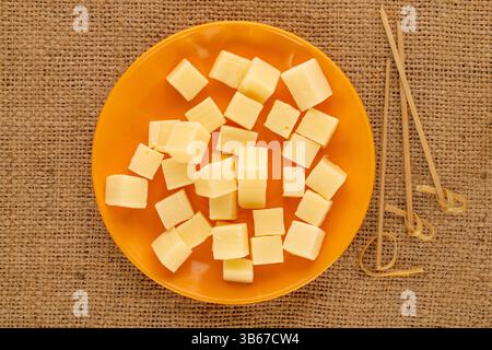 Duftender Hartkäse in Würfel geschnitten mit Bambusspießen auf einer Keramikplatte auf einem Jutetuch, Makro, Draufsicht. Stockfoto