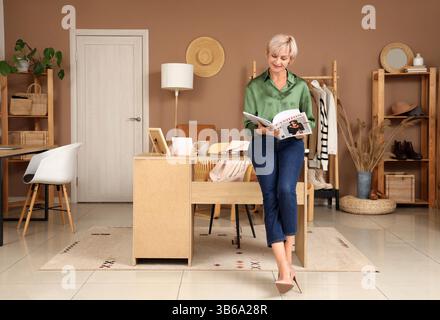 Glückliche, reife Stylistin, die Zeitschriften liest, während sie im Studio arbeitet Stockfoto