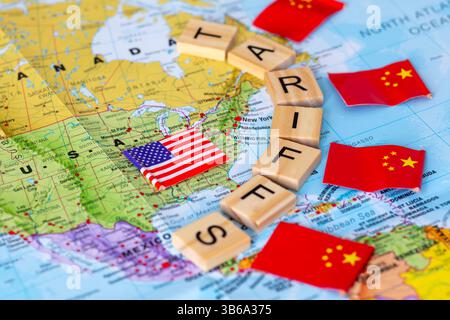 Eine Landkarte der USA, eingemauert durch Buchstaben Holzfliesen, die das Wort Zölle bilden, mit Flaggen von China draußen. Ein China-USA-Handelszölle-Konzept. Stockfoto