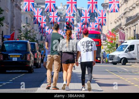 London, Großbritannien. Mai 2025. Touristen, die ein T-Shirt mit dem Aufdruck „London City 2001“ tragen, gehen durch die Regent Street. Union Flaggen (auch bekannt als Union Jack) werden hier an einem sonnigen Samstagnachmittag angezeigt, während die Menschen das lange Bankfeierwochenende genießen. Die Flaggen markieren den 80. Jahrestag des Sieges in Europa und signalisieren das Ende des Zweiten Weltkriegs. Quelle: Eleventh Photography/Alamy Live News Stockfoto