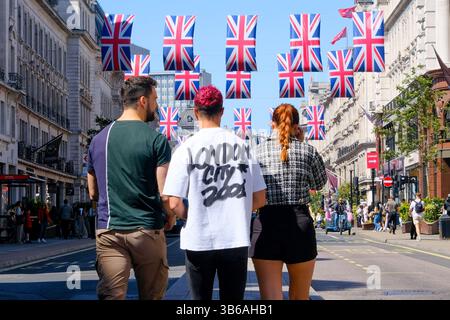 London, Großbritannien. Mai 2025. Touristen, die ein T-Shirt mit dem Aufdruck „London City 2001“ tragen, gehen durch die Regent Street. Union Flaggen (auch bekannt als Union Jack) werden hier an einem sonnigen Samstagnachmittag angezeigt, während die Menschen das lange Bankfeierwochenende genießen. Die Flaggen markieren den 80. Jahrestag des Sieges in Europa und signalisieren das Ende des Zweiten Weltkriegs. Quelle: Eleventh Photography/Alamy Live News Stockfoto