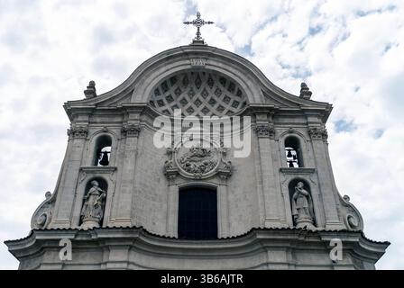 Ein detaillierter Blick auf eine Kirchenfassade mit kunstvollen architektonischen Elementen, Statuen und einem Kreuz auf der Kuppel vor einem bewölkten Himmel. Stockfoto