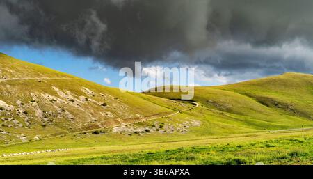 Eine malerische Landschaft mit sanften grünen Hügeln unter einem dramatischen Himmel voller dunkler Wolken. Der Pfad schlängelt sich durch die Hügel, was auf eine Ruhe hindeutet Stockfoto