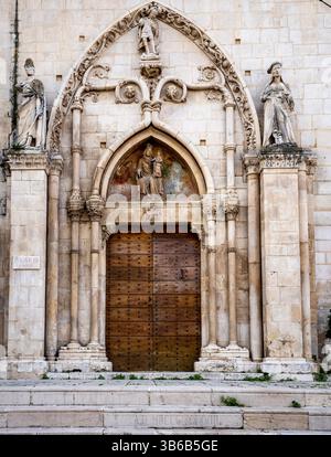 Ein historischer Steinkircheneingang mit komplizierten Schnitzereien, Heiligenstatuen und einer großen Holztür. Die Architektur zeigt gotische Elemente Stockfoto