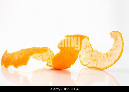 Eine spiralförmige Orangenschale liegt eingerollt auf einem sauberen weißen reflektierenden Hintergrund unter hellem Licht Stockfoto