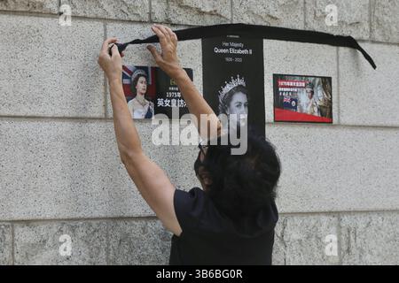 12. September 2022, HONGKONG, CHINA: Eine Frau versucht, ein schwarzes Band über die Porträts der verstorbenen britischen Königin Elizabeth II. An die Außenwand des britischen Generalkonsulats in Hongkong zu kleben, um ihre Trauer für den verstorbenen britischen Souverän auszudrücken.Sept-12.2022Hong Kong.ZUMA/Liau Chung-ren (Kreditbild: © Liau Chung-ren/ZUMA Press Wire) Stockfoto