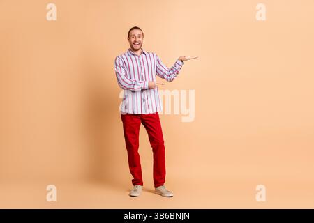Selbstbewusstes Männermodell mit lässigem gestreiftem Hemd und leuchtend roter Hose vor beigefarbenem Hintergrund Stockfoto