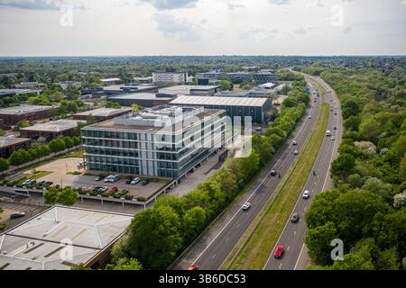 Blick aus der Vogelperspektive auf ein modernes Bürogebäude aus Glas in einem Business Park, neben einer vielspurigen Autobahn, umgeben von Bäumen und anderen Geschäftsbereichen Stockfoto