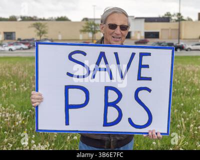 Bürger der unteilbaren Iowa-Bewegung nahmen am 3. Mai 2025 an der Demonstration zum Nationalfeiertag in West Burlington, Iowa, USA, Teil. Ein Mann hielt ein "Save PBS"-Schild. Stockfoto