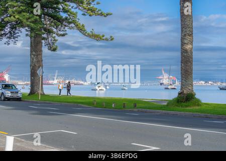 Tauranga Neuseeland - 26. Juni 2023; Blick von der Pilot Bay auf beide Seiten des Hafens von Tauranga Einrichtungen und Boote im Hafen mit Fußgängern auf dem Weg. Stockfoto