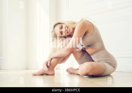 Ein Porträt einer Blondine, die Yoga macht und auf dem Boden sitzt, mit dem Kopf auf dem Knie Stockfoto