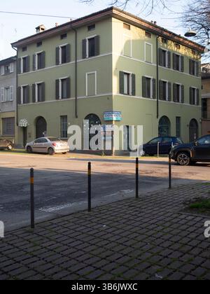 Cremona, Italien - 12. April 2025 Außenansicht eines Wohngebäudes mit olivgrüner Fassade, Bogenfenstern, dunklen Fensterläden und in der Nähe geparkten Autos Stockfoto