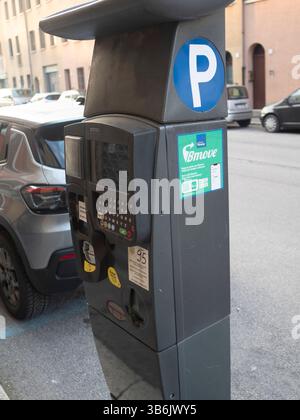 Cremona, Italien - 12. April 2025 Nahaufnahme eines grauen Parkautomaten auf einer Straße mit Autos wie Grey 2023 Nissan Rogue SUV und Dark Small Hatchback Stockfoto