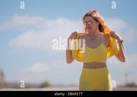 Porträt einer schönen erwachsenen Frau in blonden Haaren und Sportbekleidung vor dem blauen Himmel. Morgens joggen, Sport treiben. Stockfoto