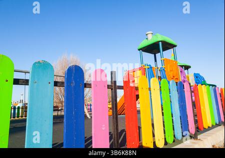Der Kinderspielplatz ist mit einem mehrfarbigen Zaun umzäunt. Stockfoto
